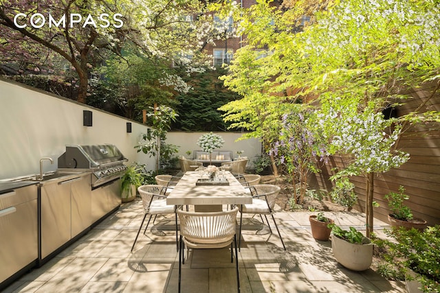 view of patio featuring area for grilling, a sink, a fenced backyard, an outdoor kitchen, and outdoor dining space