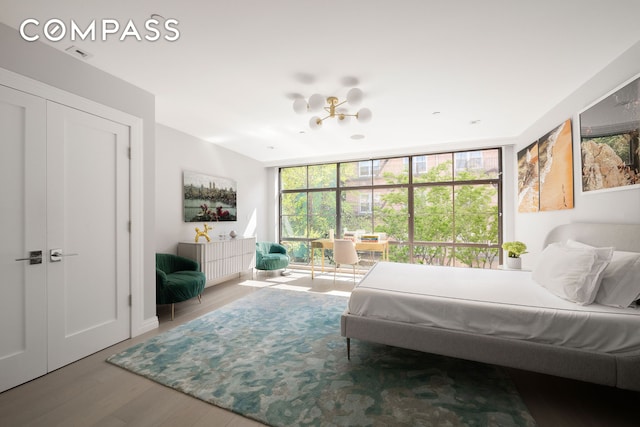 bedroom with a chandelier, visible vents, expansive windows, and wood finished floors