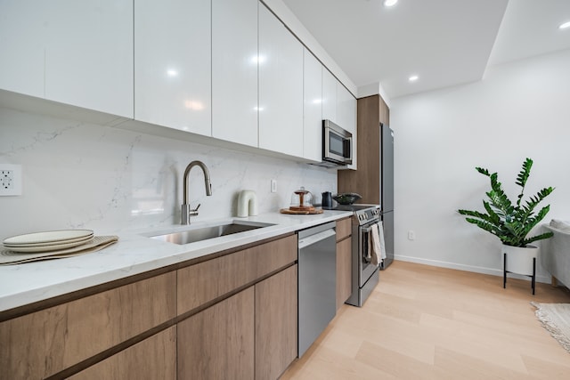 11-52 44th Dr Unit 3-A, New York City, NY 11101 - kitchen featuring appliances with stainless steel finishes, a sink, backsplash, light wood-type flooring, and light stone countertops