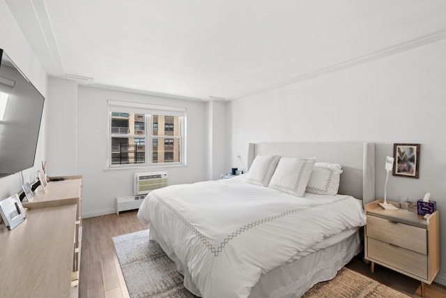bedroom with baseboard heating, baseboards, a wall mounted AC, and wood finished floors