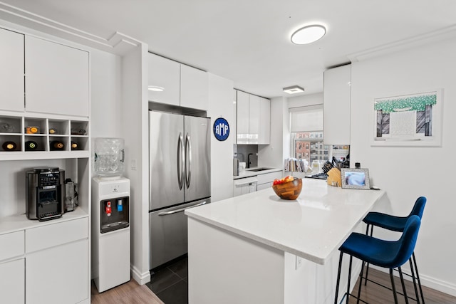 kitchen with stainless steel refrigerator, a sink, a peninsula, white cabinetry, and a kitchen bar