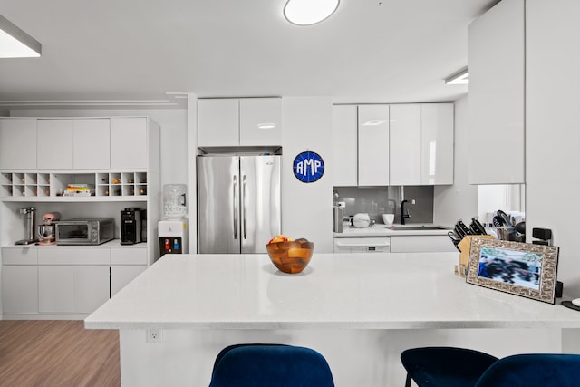 kitchen featuring stainless steel refrigerator, modern cabinets, a kitchen bar, white cabinetry, and a sink