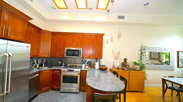 kitchen with a sink, stainless steel appliances, a peninsula, tasteful backsplash, and visible vents