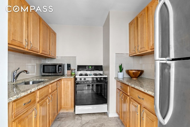 kitchen with backsplash, light stone countertops, appliances with stainless steel finishes, and a sink