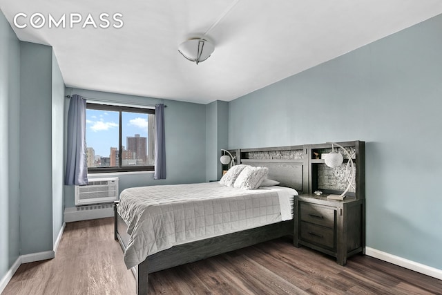 bedroom featuring an AC wall unit, baseboards, wood finished floors, and a city view