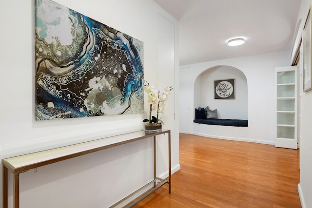 hall with arched walkways, baseboards, and wood finished floors
