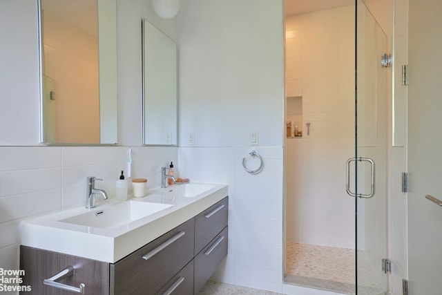 bathroom with double vanity, tile walls, a sink, and a stall shower