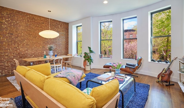 living area with baseboards, brick wall, plenty of natural light, and wood finished floors