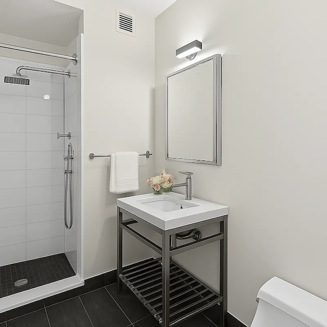 full bathroom featuring toilet, tiled shower, vanity, tile patterned flooring, and baseboards