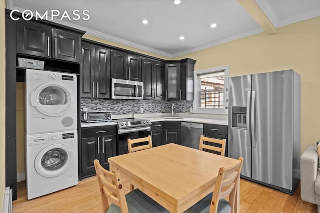 kitchen featuring crown molding, stacked washing maching and dryer, a sink, dark cabinetry, and stainless steel appliances