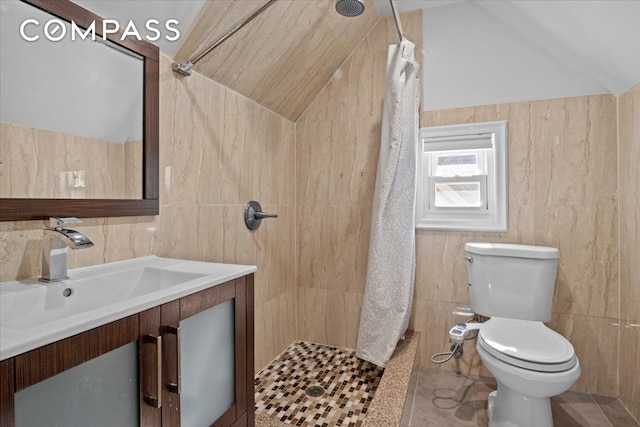 full bath with a tile shower, vanity, toilet, tile walls, and vaulted ceiling