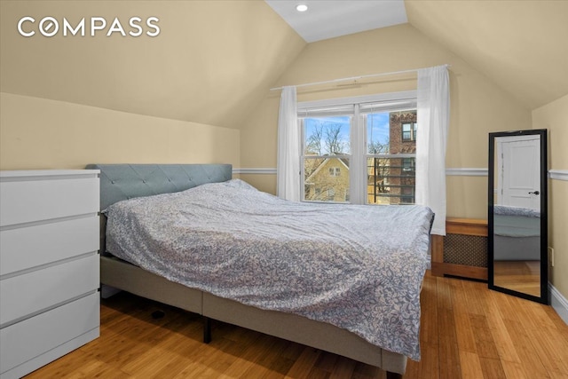 bedroom featuring baseboards, wood finished floors, and lofted ceiling