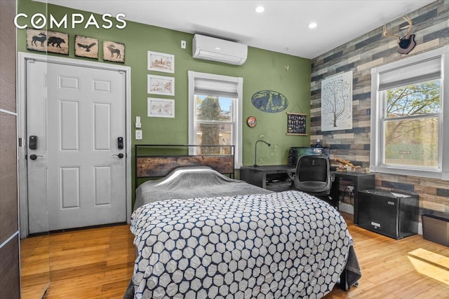 bedroom featuring multiple windows, a wall unit AC, an accent wall, and wood finished floors