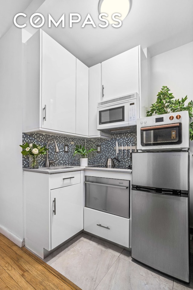 kitchen featuring white microwave, light countertops, white cabinetry, a sink, and a warming drawer