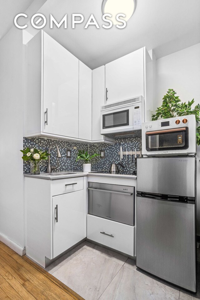 335 W 21st St Unit 3Re, New York City, NY 10011 - kitchen featuring white microwave, a sink, white cabinets, light countertops, and a warming drawer