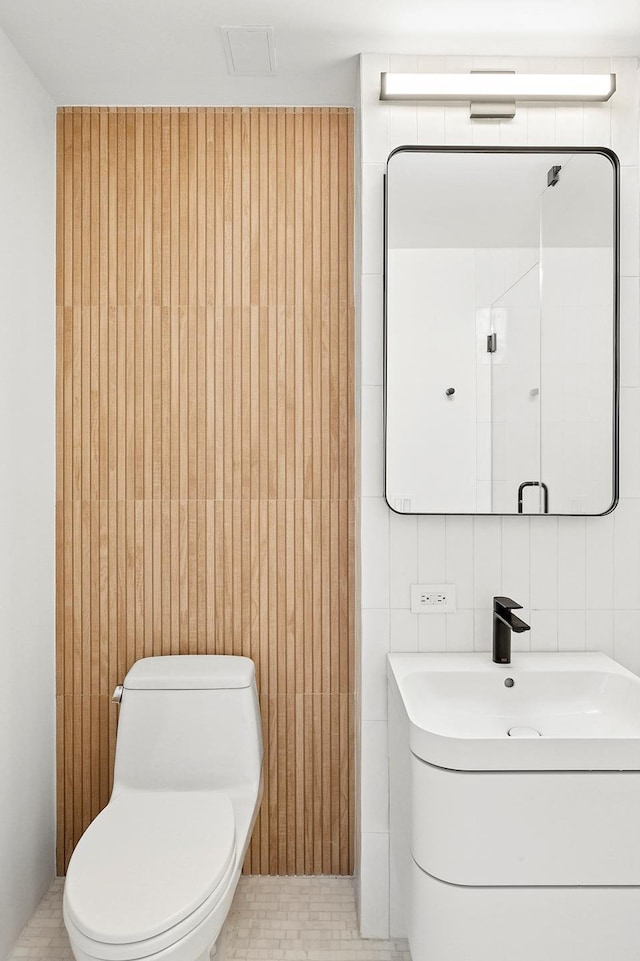 bathroom featuring toilet, tile walls, and vanity