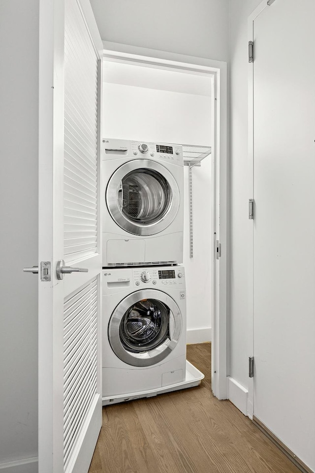clothes washing area with stacked washer and clothes dryer and wood finished floors