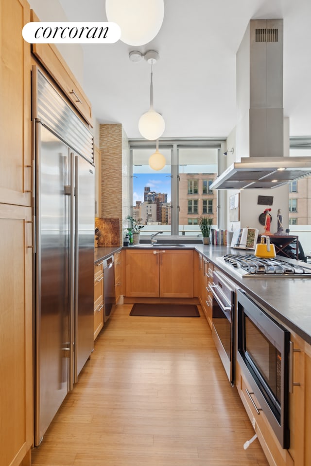 kitchen featuring island exhaust hood, built in appliances, dark countertops, and light wood-type flooring
