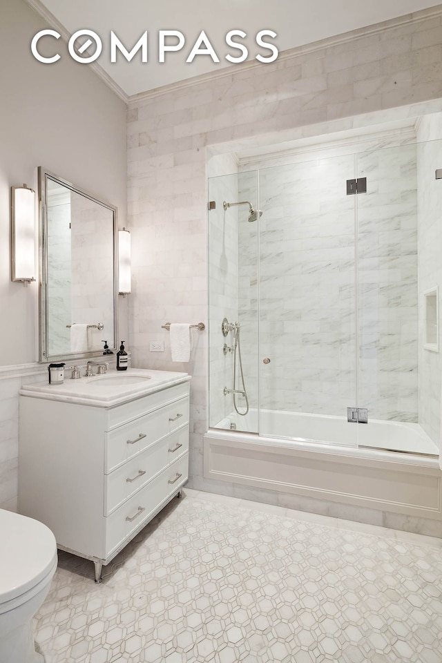 bathroom featuring vanity, toilet, tile walls, combined bath / shower with glass door, and ornamental molding