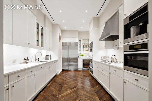 kitchen with a sink, wall chimney exhaust hood, stainless steel appliances, white cabinetry, and glass insert cabinets
