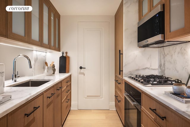 kitchen with light stone counters, a sink, light wood-style floors, brown cabinetry, and stainless steel appliances