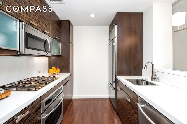 kitchen with appliances with stainless steel finishes, a sink, baseboards, light countertops, and dark wood-style floors