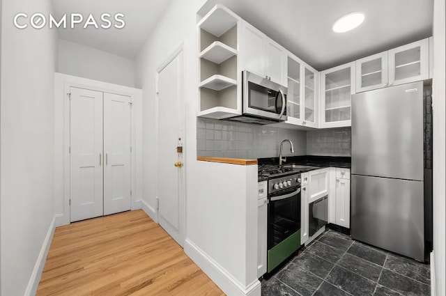 130 W 80th St Unit 4F, New York City, NY 10024 - kitchen with appliances with stainless steel finishes, white cabinetry, decorative backsplash, open shelves, and glass insert cabinets