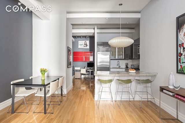 kitchen featuring light wood finished floors, a peninsula, baseboards, stainless steel built in fridge, and a kitchen bar