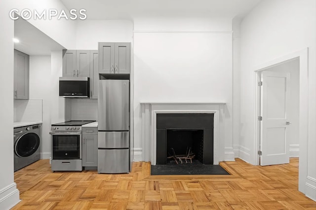 62 W 87th St Unit 1F, New York City, NY 10024 - kitchen with washer / clothes dryer, appliances with stainless steel finishes, gray cabinetry, and a fireplace with flush hearth