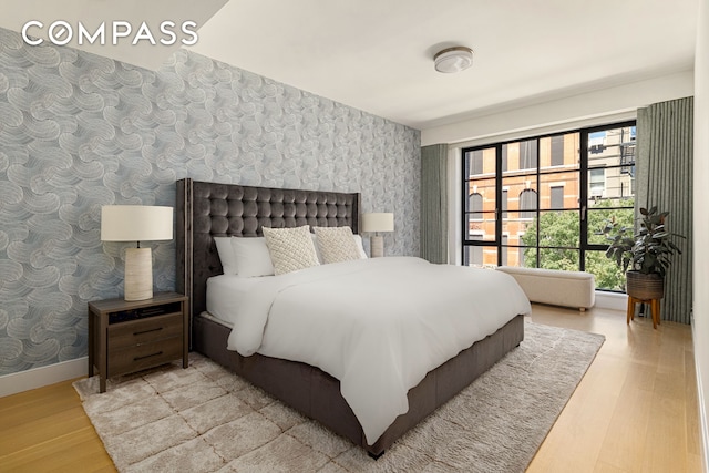 bedroom with baseboards, wood finished floors, and wallpapered walls