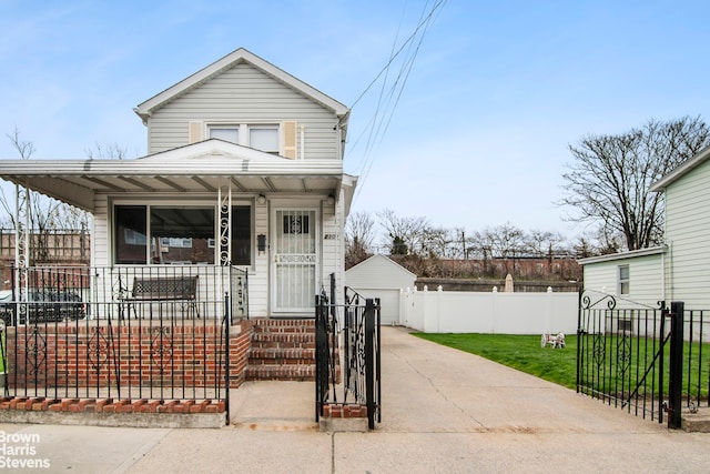 shotgun-style home featuring a porch, driveway, a fenced front yard, a front yard, and a detached garage
