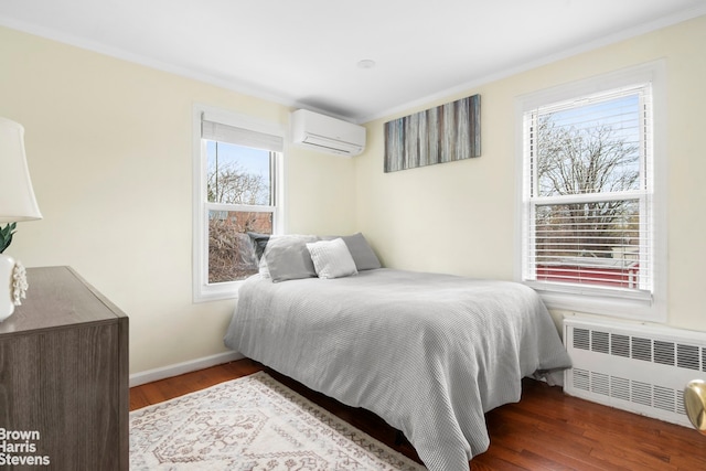 bedroom with a wall unit AC, wood finished floors, baseboards, radiator, and ornamental molding