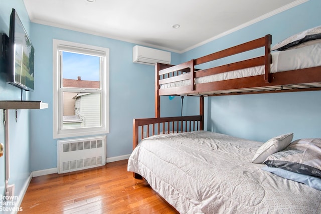 bedroom with crown molding, hardwood / wood-style floors, baseboards, radiator heating unit, and a wall mounted AC