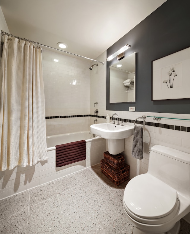 bathroom with toilet, tile walls, a wainscoted wall, tiled shower / bath combo, and a sink