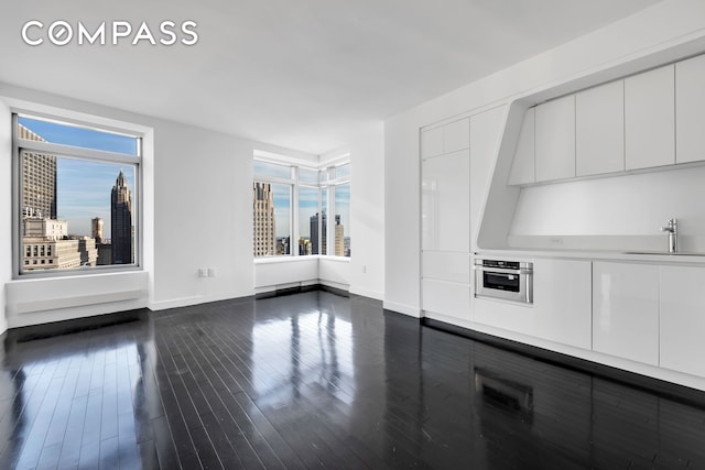 123 Washington St Unit 52F, New York City, NY 10006 - unfurnished living room featuring a sink, baseboards, healthy amount of natural light, and dark wood-style flooring