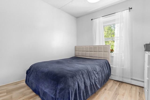 bedroom with a baseboard heating unit and wood finished floors