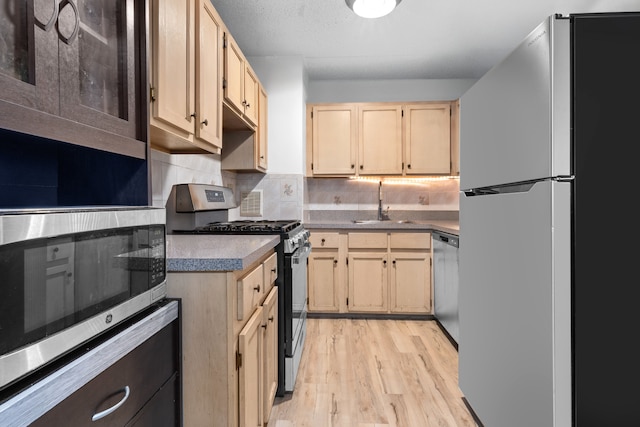 kitchen with tasteful backsplash, light wood-type flooring, a sink, light brown cabinets, and stainless steel appliances
