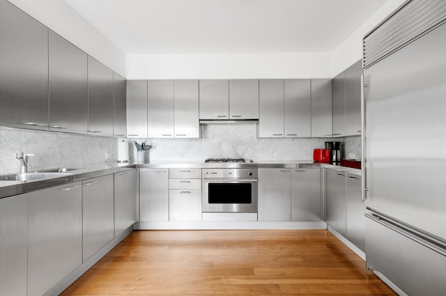 kitchen featuring stainless steel countertops, light wood-style floors, under cabinet range hood, a sink, and appliances with stainless steel finishes