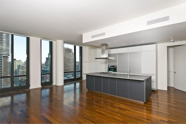 kitchen featuring wall chimney exhaust hood, modern cabinets, dark wood-style flooring, a sink, and stovetop