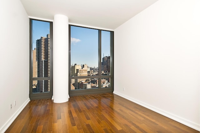 empty room featuring expansive windows, wood finished floors, a view of city, and baseboards
