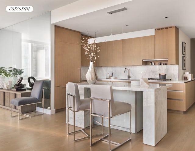 kitchen with a kitchen island, tasteful backsplash, modern cabinets, a sink, and light wood-style floors
