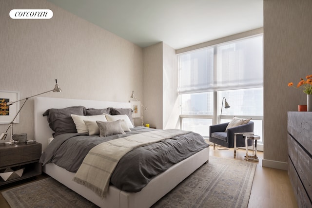 bedroom featuring wallpapered walls, multiple windows, and wood finished floors