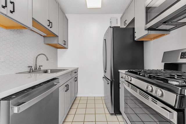 kitchen with decorative backsplash, appliances with stainless steel finishes, a sink, light countertops, and light tile patterned flooring