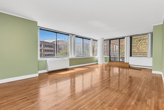 empty room with wood-type flooring, ornamental molding, baseboards, and radiator heating unit