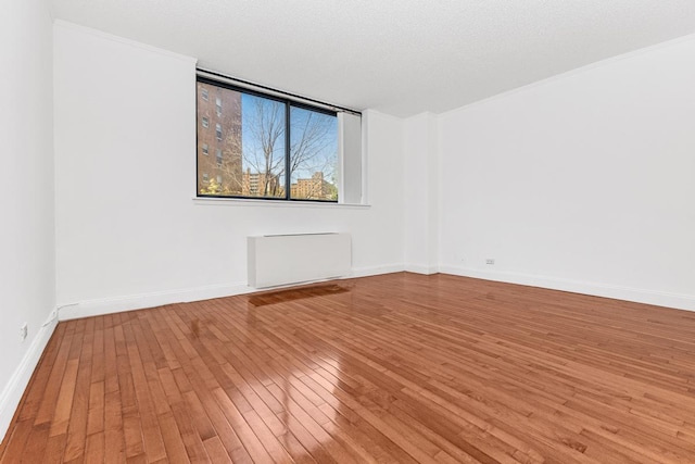 empty room with baseboards, crown molding, radiator heating unit, and hardwood / wood-style flooring