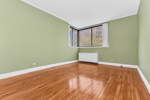 empty room with baseboards, ornamental molding, radiator heating unit, and hardwood / wood-style floors