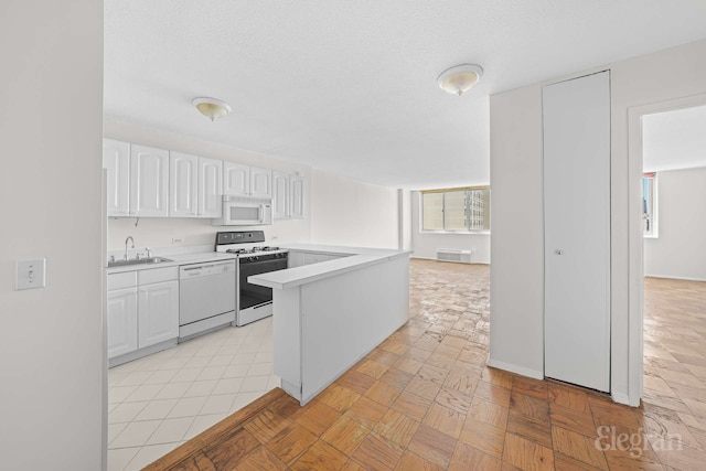 kitchen featuring white appliances, white cabinets, a sink, and light countertops