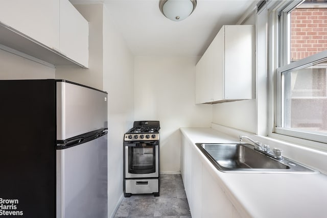 kitchen with white cabinets, appliances with stainless steel finishes, a sink, light countertops, and baseboards