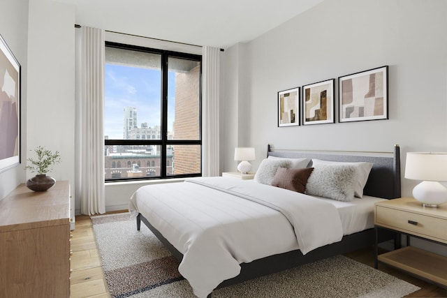 bedroom with a view of city, multiple windows, and light wood finished floors