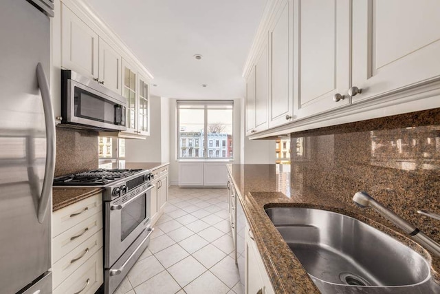 kitchen with appliances with stainless steel finishes, white cabinetry, a sink, dark stone counters, and light tile patterned flooring